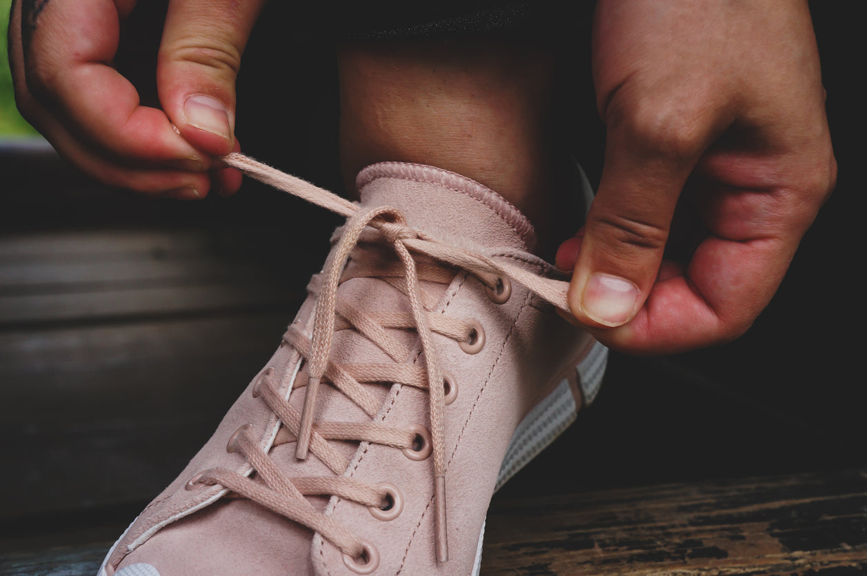 Primo piano di una scarpa da ginnastica rosa mentre i lacci vengono annodati in un fiocco.