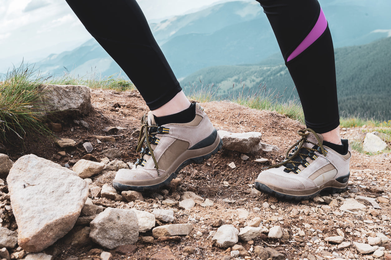 Primo piano di scarponi da montagna mentre una persona fa un passo su un sentiero roccioso, con il focus sulla suola e sulla presa delle scarpe.