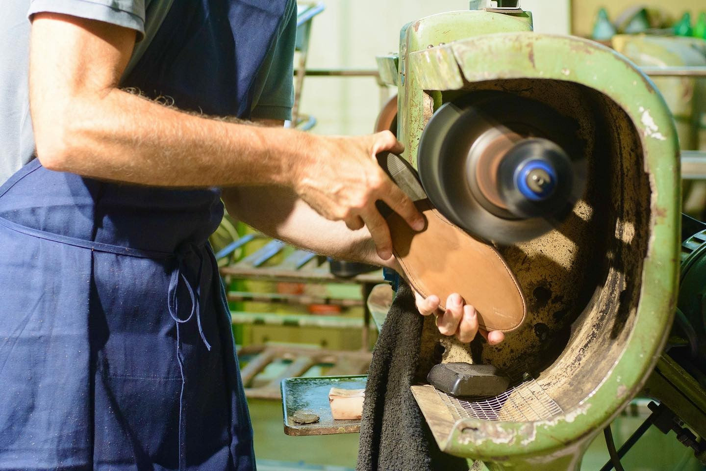 Foto von der Herstellung eines Maßschuhs, auf dem ein Handwerker den Boden des Schuhs mit einer Schleifmaschine bearbeitet. Der Fokus liegt auf dem Schleifprozess.